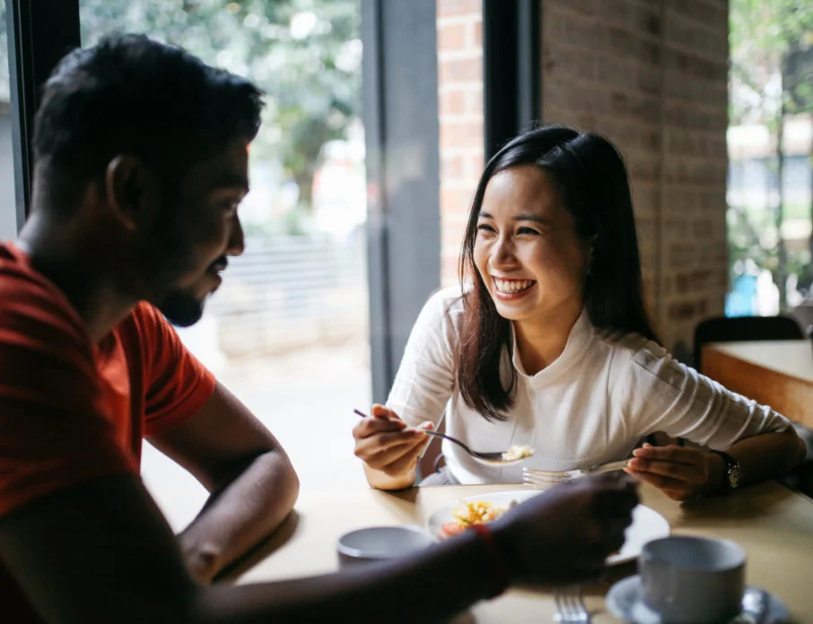 Young couple at a restaurant laughing and smiling together as they ask each other first date questions.
