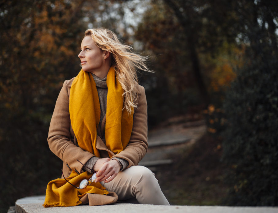 Blonde woman sitting outdoors and looking out into the distance while thinking about how to break up with someone you love.