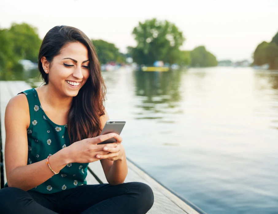 Happy young woman smiling while using her phone and trying out some dating message tips.