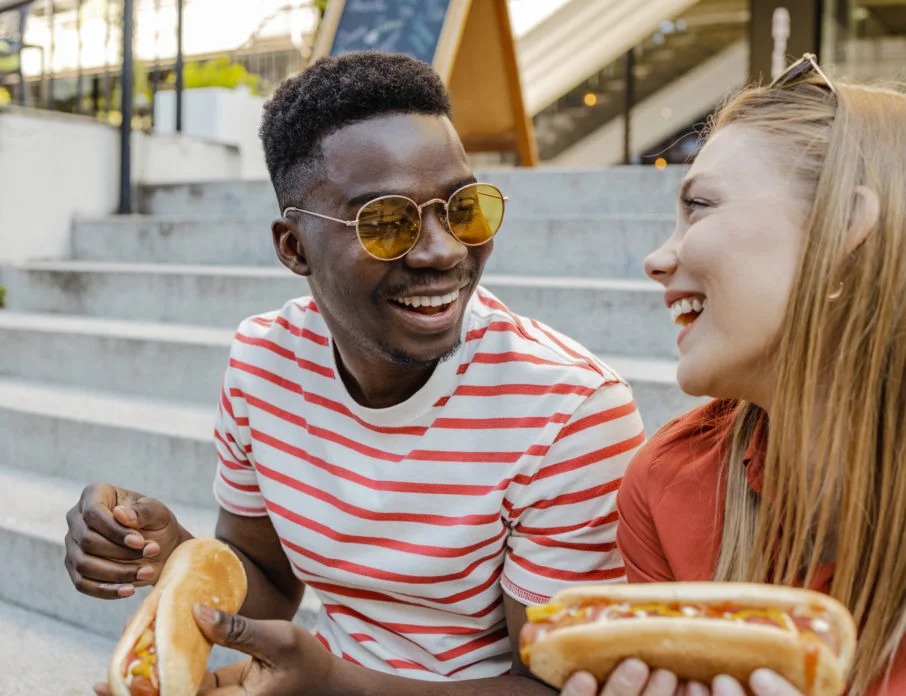 Young African American man and Caucasian woman on a first date, eating a hot dog on the street and laughing while getting over their first date nerves.