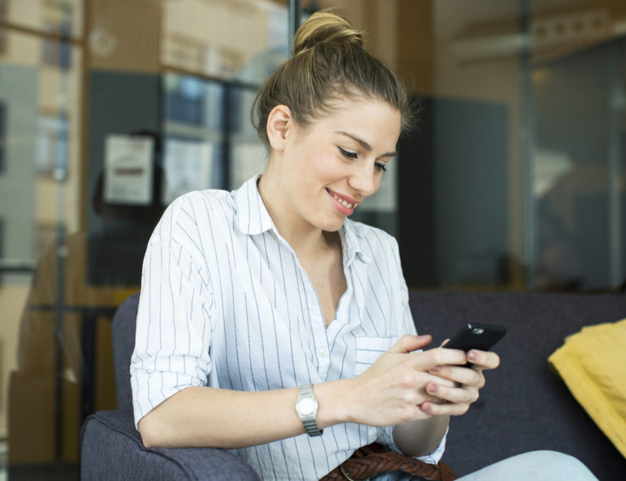 Happy, smiling woman using mobile phone to practice ways of how to flirt over text.