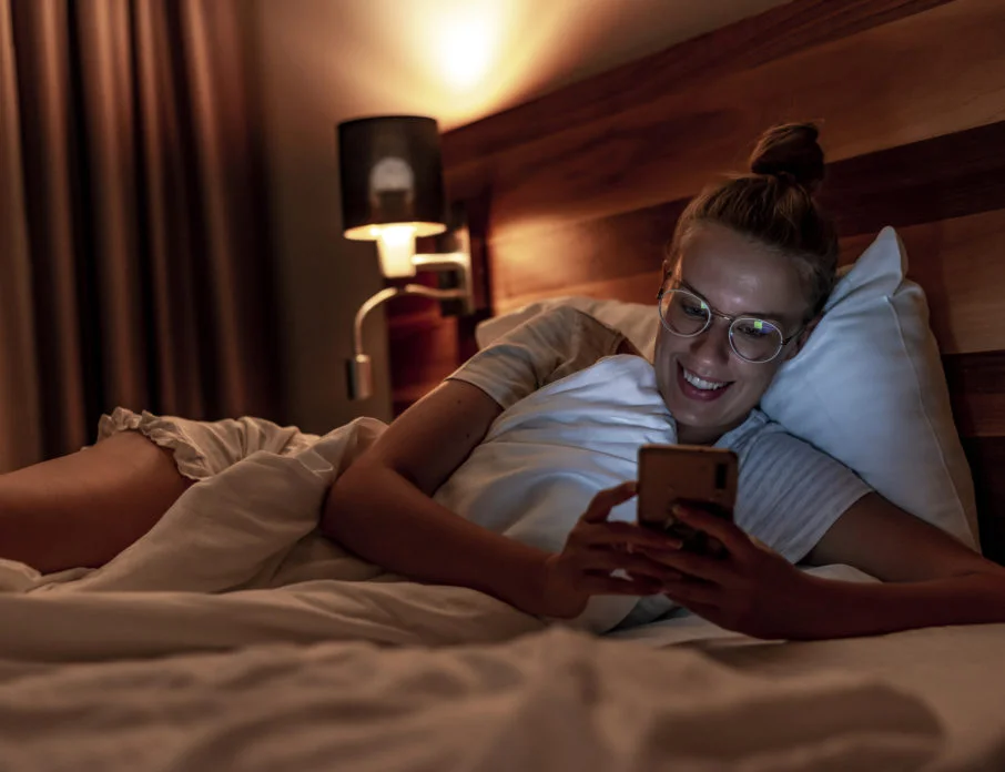 Smiling woman lying in bed and looking at mobile phone after receiving a goodnight love message.