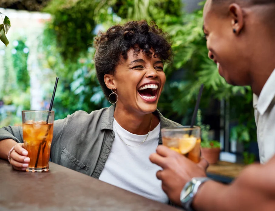Happy couple sitting in an outdoor bar and laughing together while enjoying a good second date idea.