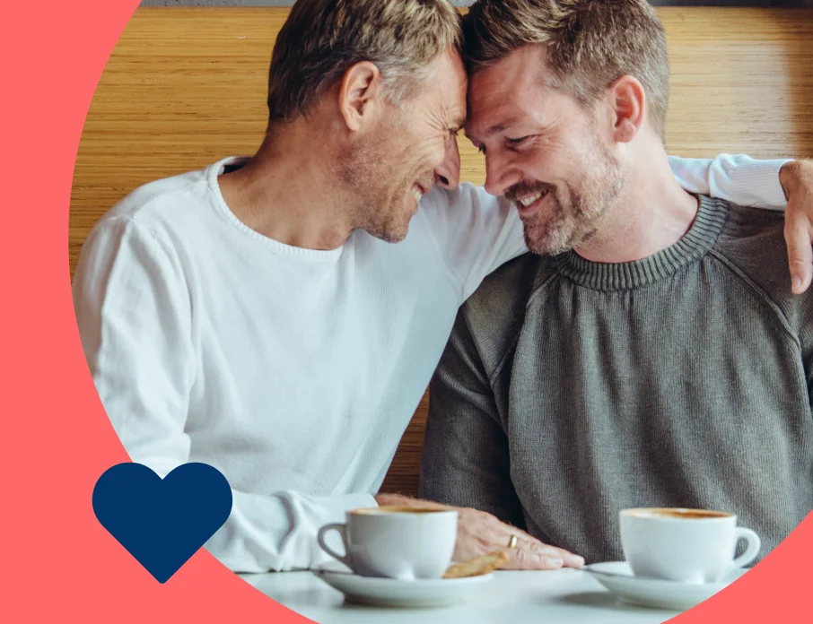 Two men smiling and embracing each other while enjoying a coffee date.