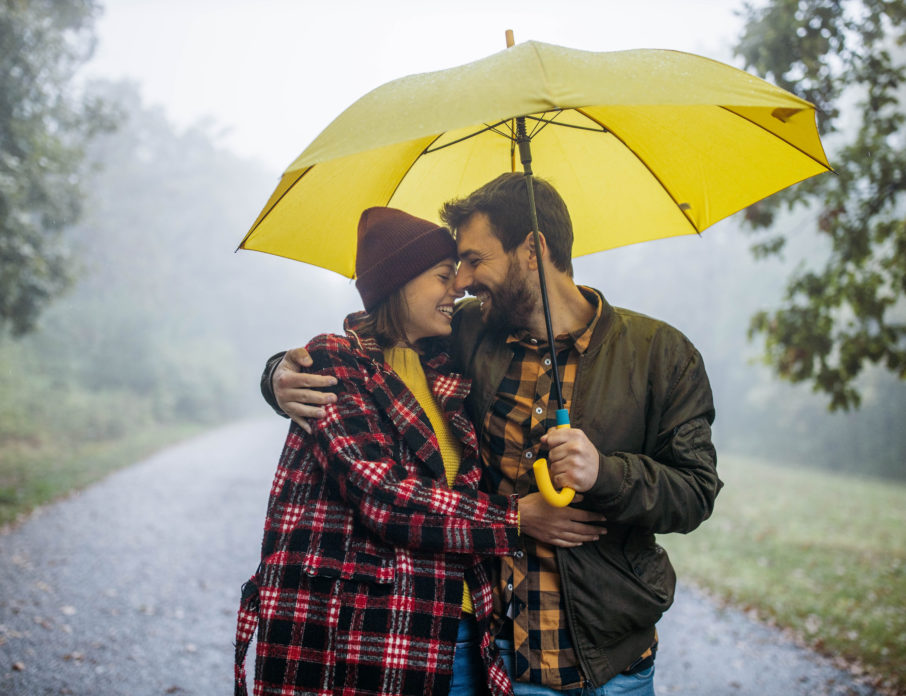 Happy embraced couple taking a walk in the forest on a rainy day at forest and smiling as they share some different ways to say I love you.