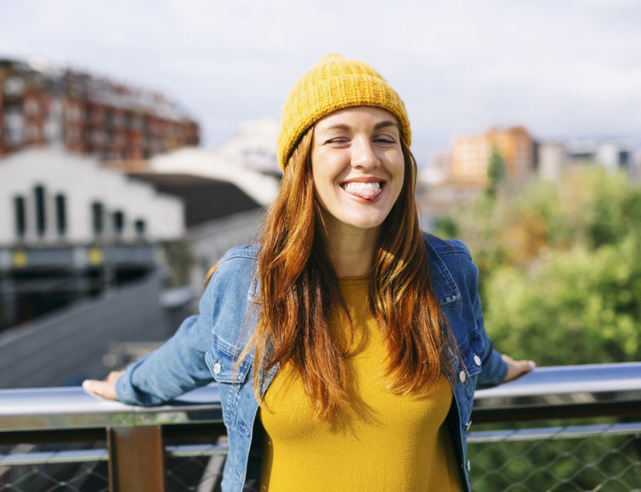 Smiling young woman standing outdoors on a bridge and looking happily at the camera after practicing positive self-talk.