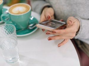 Woman using mobile phone while having a coffee to check is Bumble free?