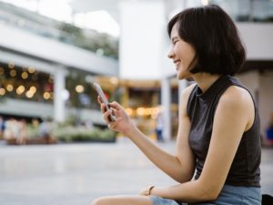 Attractive woman looking at mobile phone and laughing at clever tinder pick up line