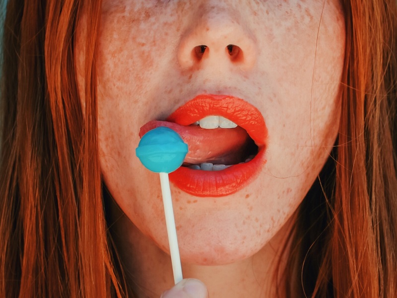 attractive red head woman licking a popsicle as the definition of flirting