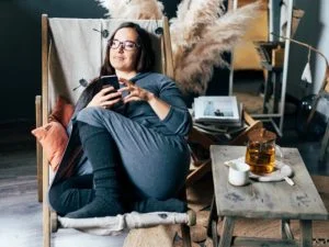 woman sitting at home in chair holding phone and texting flirty questions to ask a guy