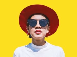 woman with red hat standing in front of yellow wall challenging her limiting beliefs