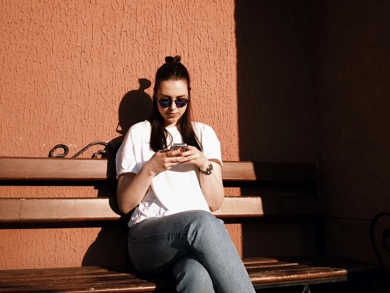 woman sitting on a bench typing her best hinge answers on her mobile phone