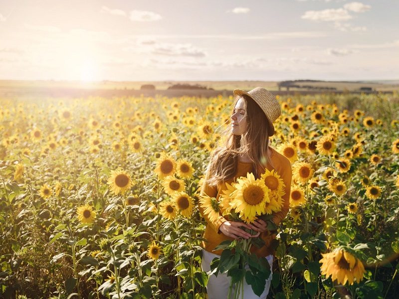 single woman standing in field of sunflowers