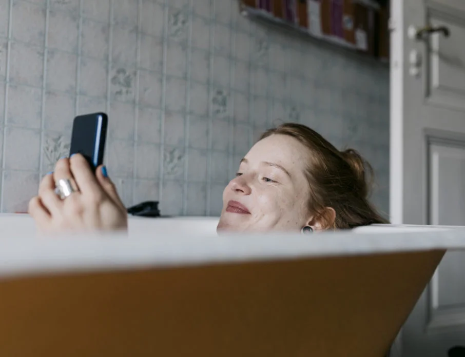 Woman in bath smiling and texting funny response to "what's up" message.