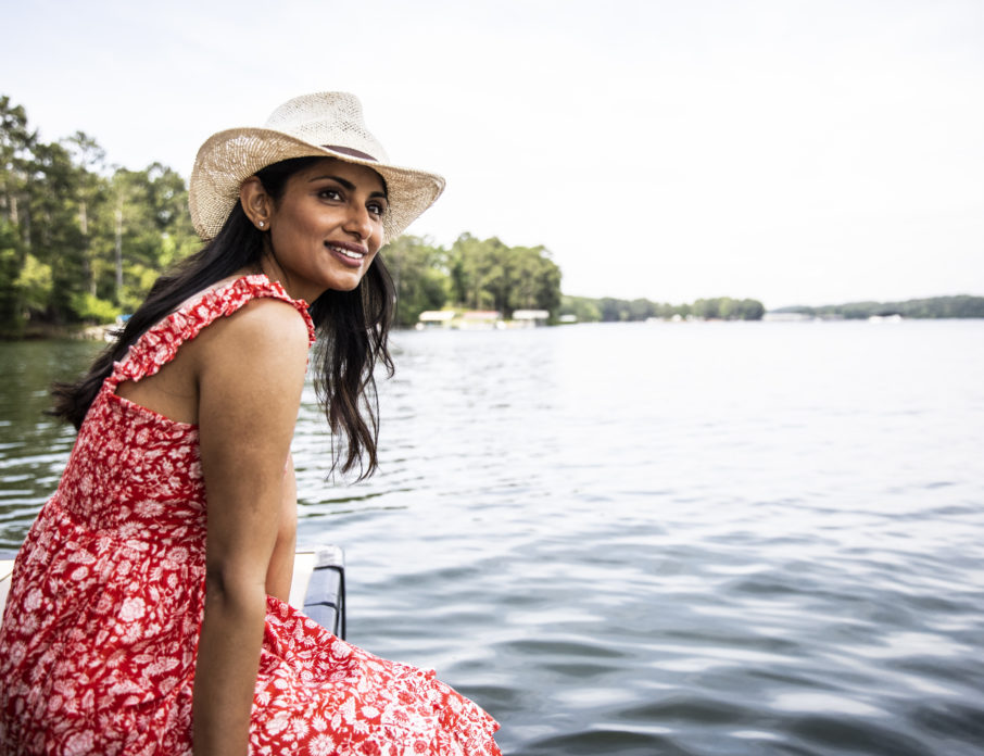 Woman sitting down next to water, smiling and thinking about how to enjoy single life.