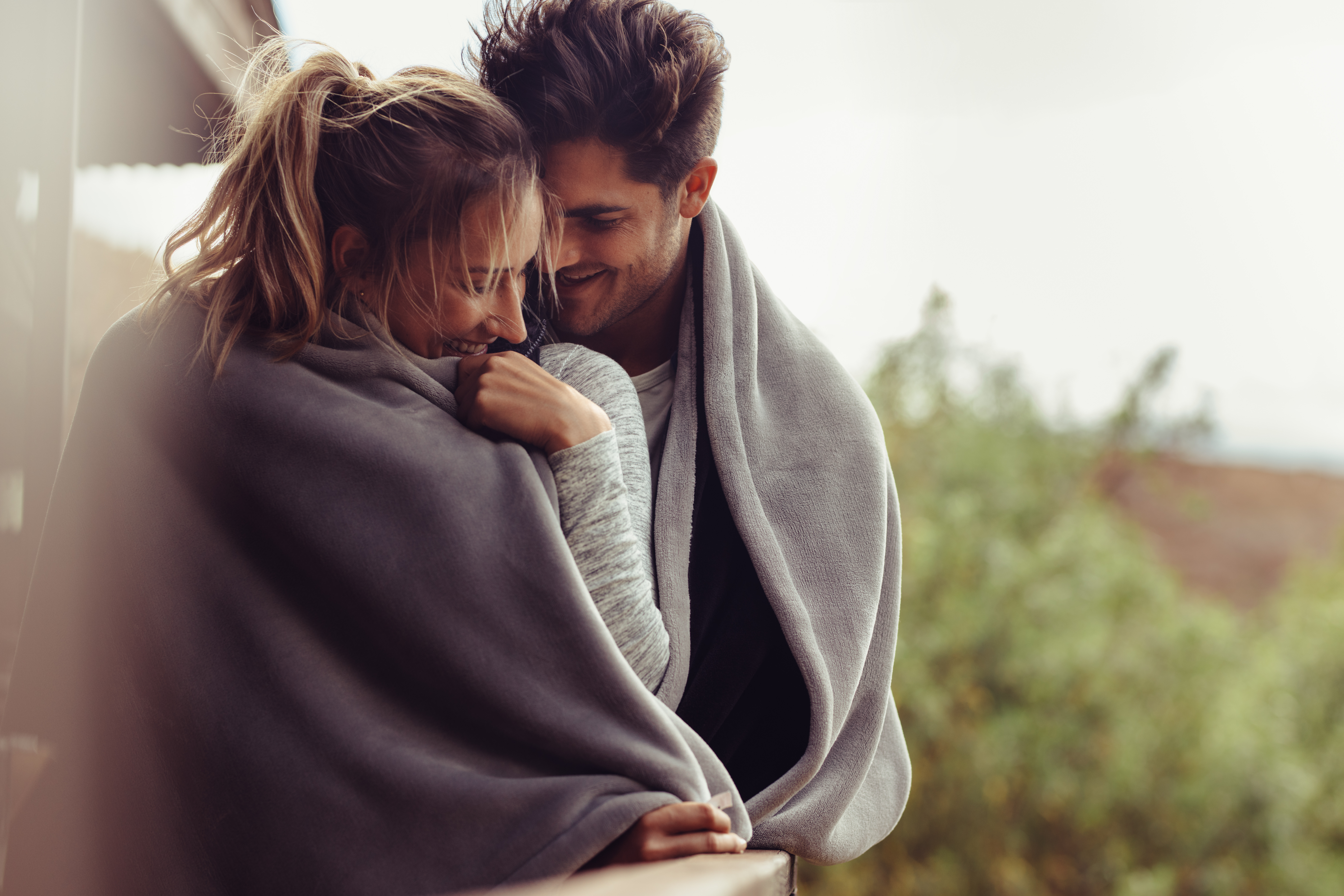 Couple cuddling together outside during winter, wrapped in blankets and enjoying cuffing season.