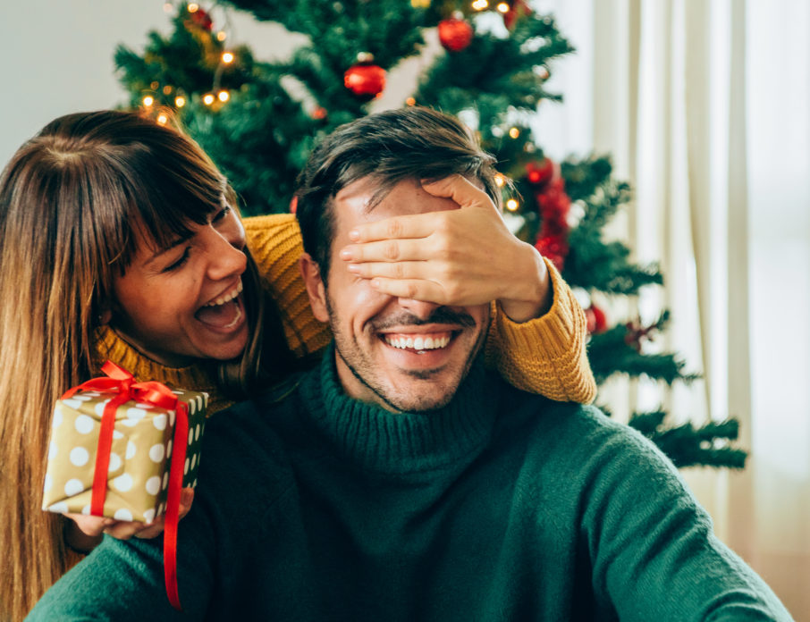 Happy couple smiling and laughing together while exchanging their cute Christmas gift ideas.