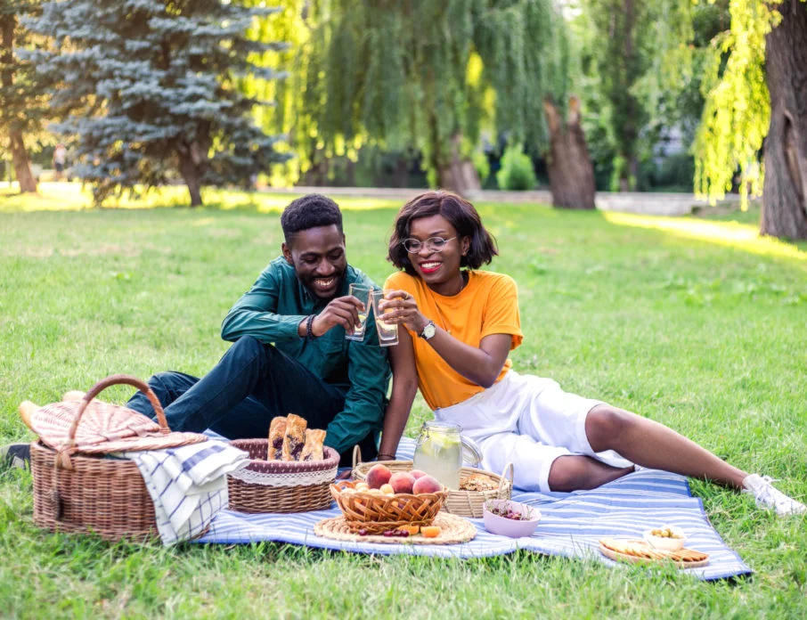 Young couple smiling together while having a picnic in the park as an easy first date idea.