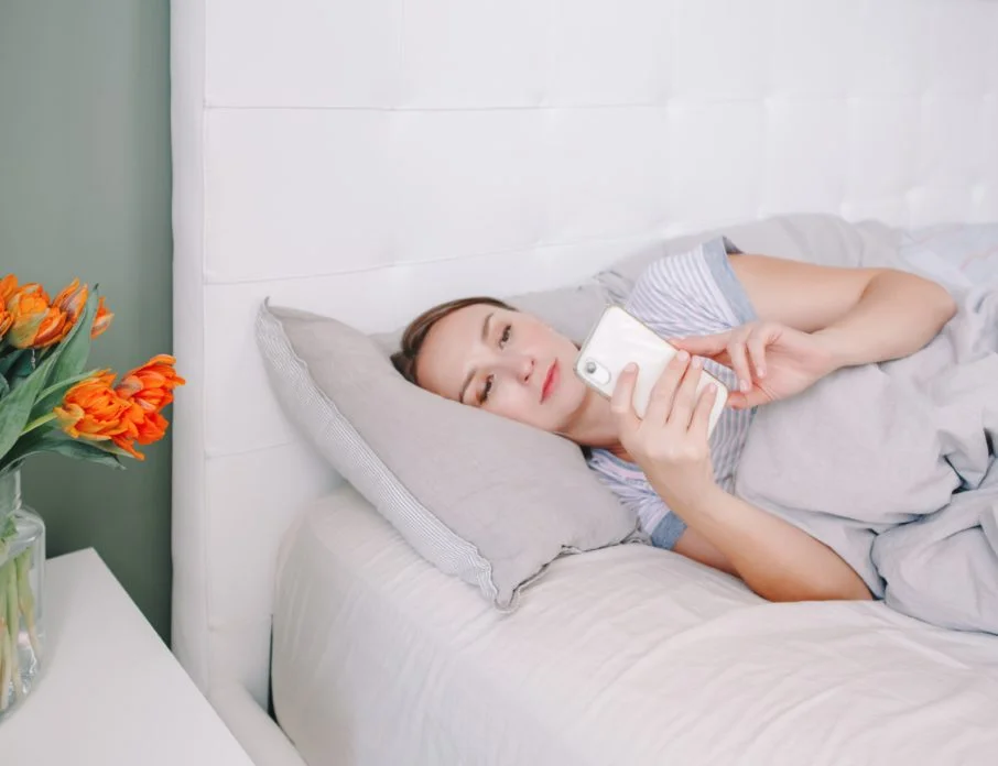 Smiling woman lying in bed on her phone reading a good morning paragraph for her from her partner.
