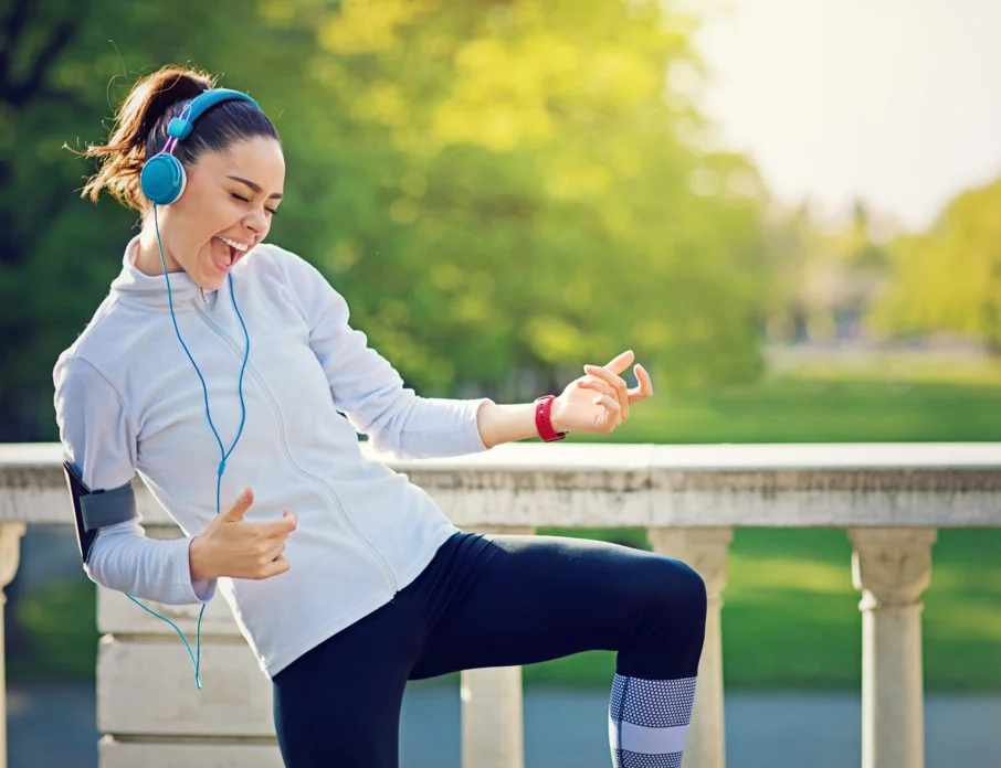 Happy woman wearing headphones and dancing while listening to songs about strong women.