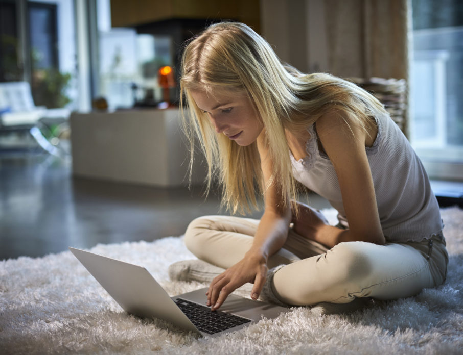 Young woman sitting on carpet at home using laptop while practicing tips for tackling dating app fatigue.