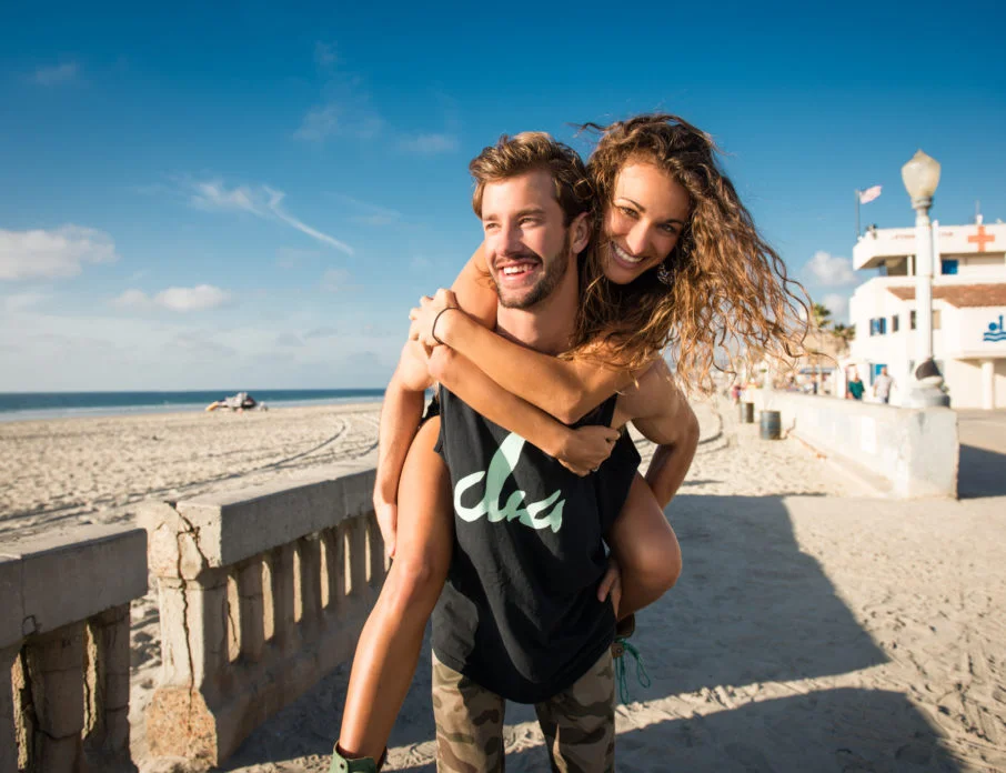 Young man giving girlfriend a piggy back at the beach while enjoying the best date ideas in San Diego.