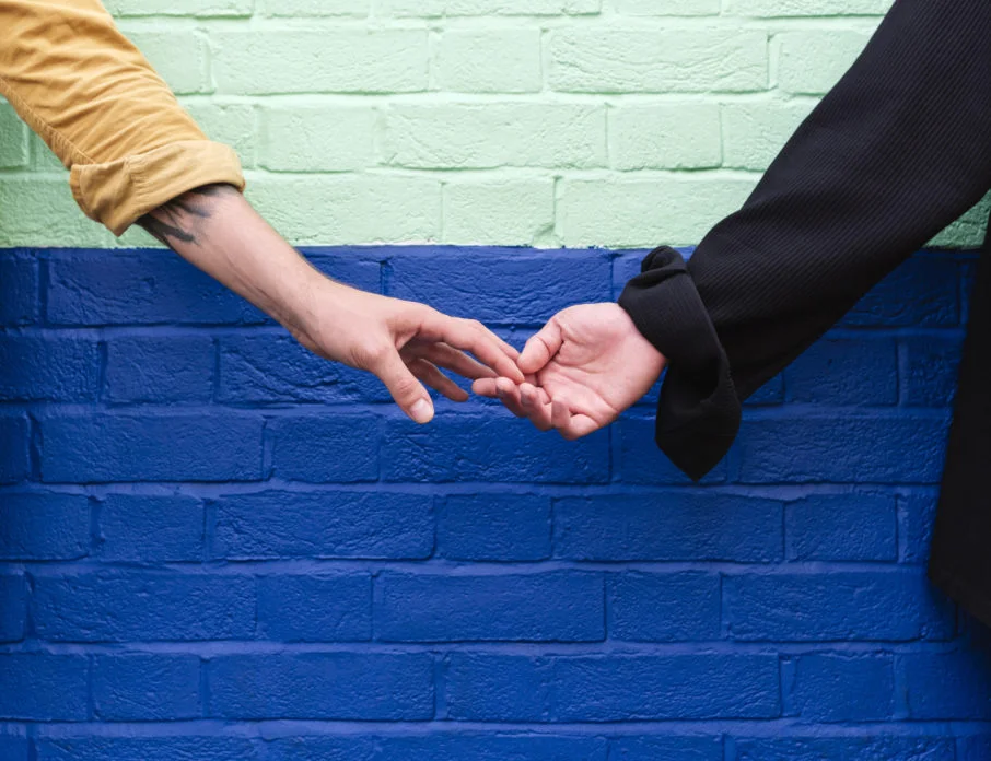 Couple holding hands in front of colorful wall after meeting in one of the best cities for dating in your 40s.