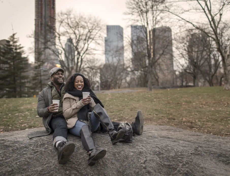 Smiling couple on a date, sitting on a rock outdoors and enjoying one of the most romantic things to do in NYC.