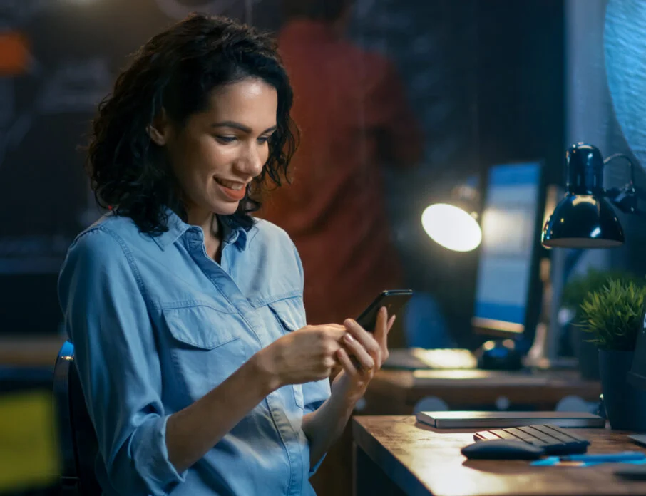 Woman at her work station looking at a smartphone.