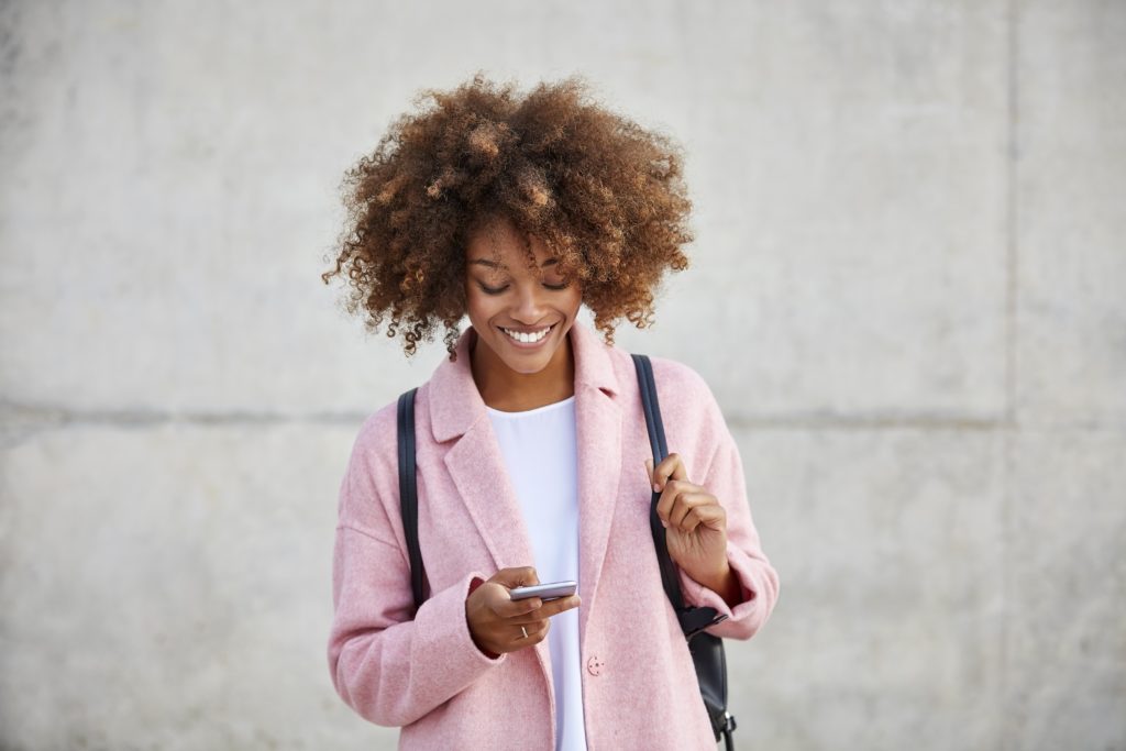 attractive single woman wearing pink coat using her mobile for online dating