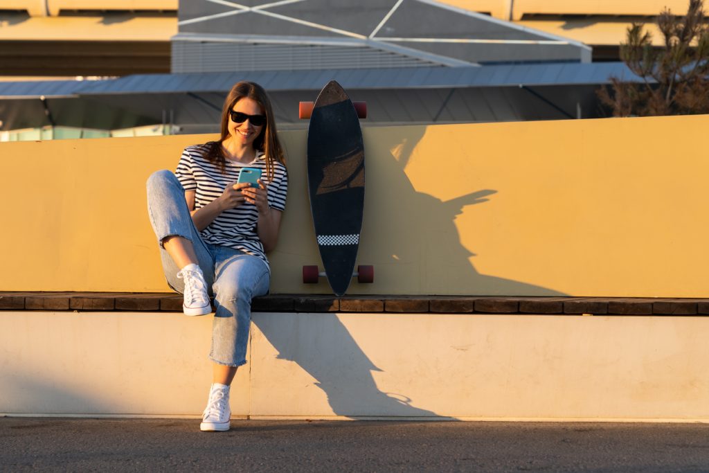 Woman sitting down in the sunshine, smiling and using smartphone to find other Miami singles.