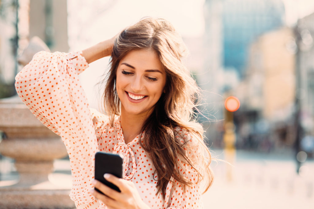 Young woman smiling while using her mobile phone to meet other Christian singles online.