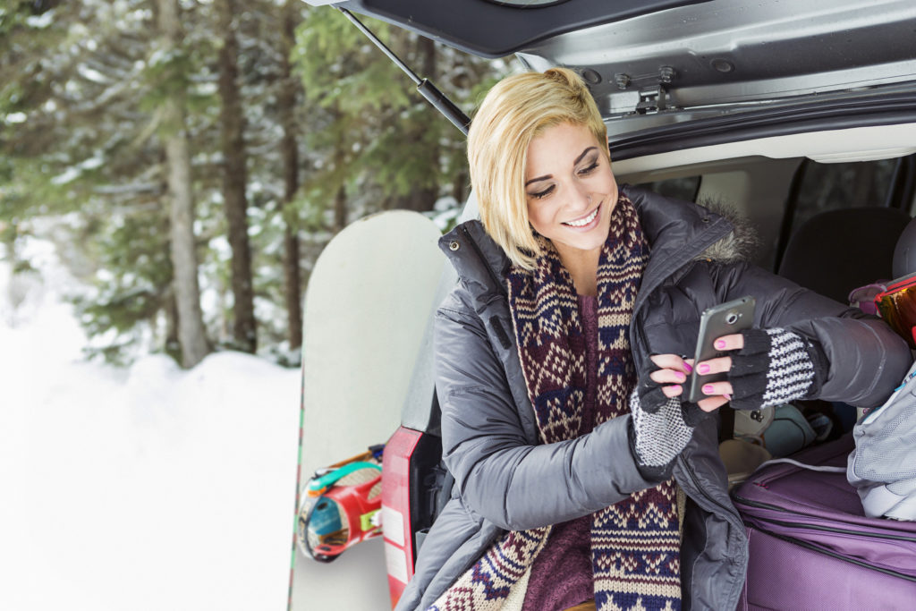 Happy woman smiling and leaning against car and texting while online dating in Alaska.