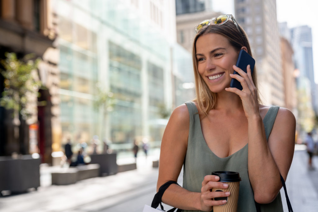Happy American single woman smiling and using mobile phone outdoors.
