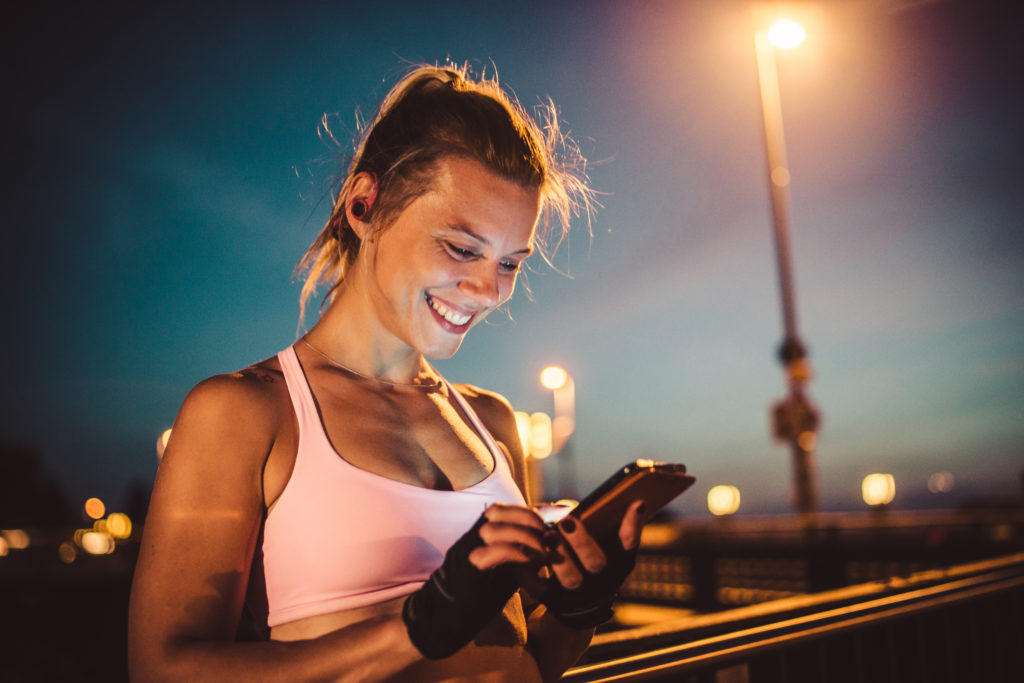 Smiling woman after a workout using her smartphone to find other women seeking women through online dating.