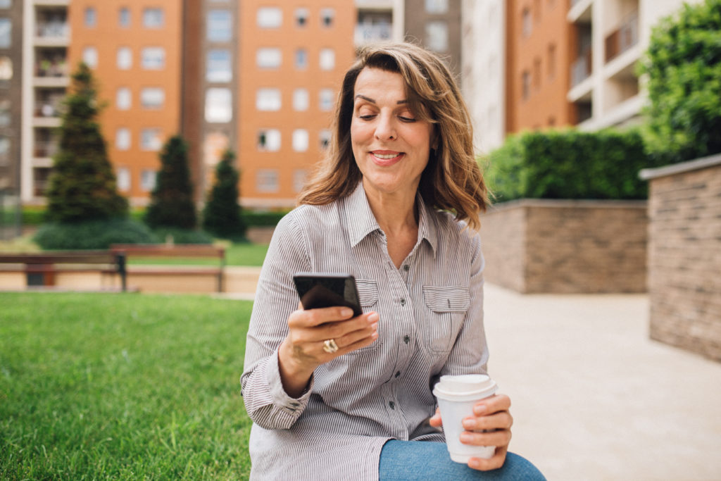 Mature woman sitting on bench, smiling and using mobile phone while online dating.