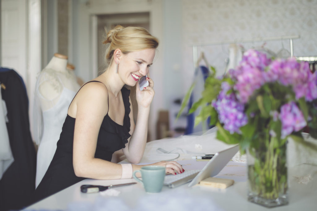 Happy, smiling woman using laptop and speaking on mobile phone while meeting other marriage-minded people online.
