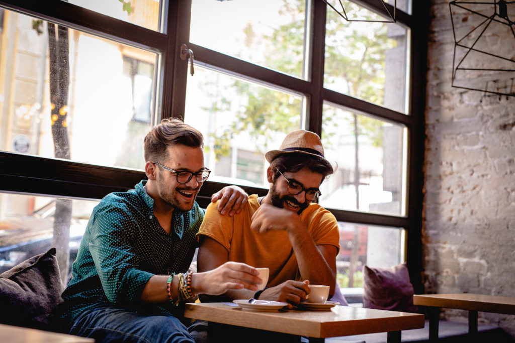 Two happy, smiling men laughing together in a café and enjoying LGBT dating.