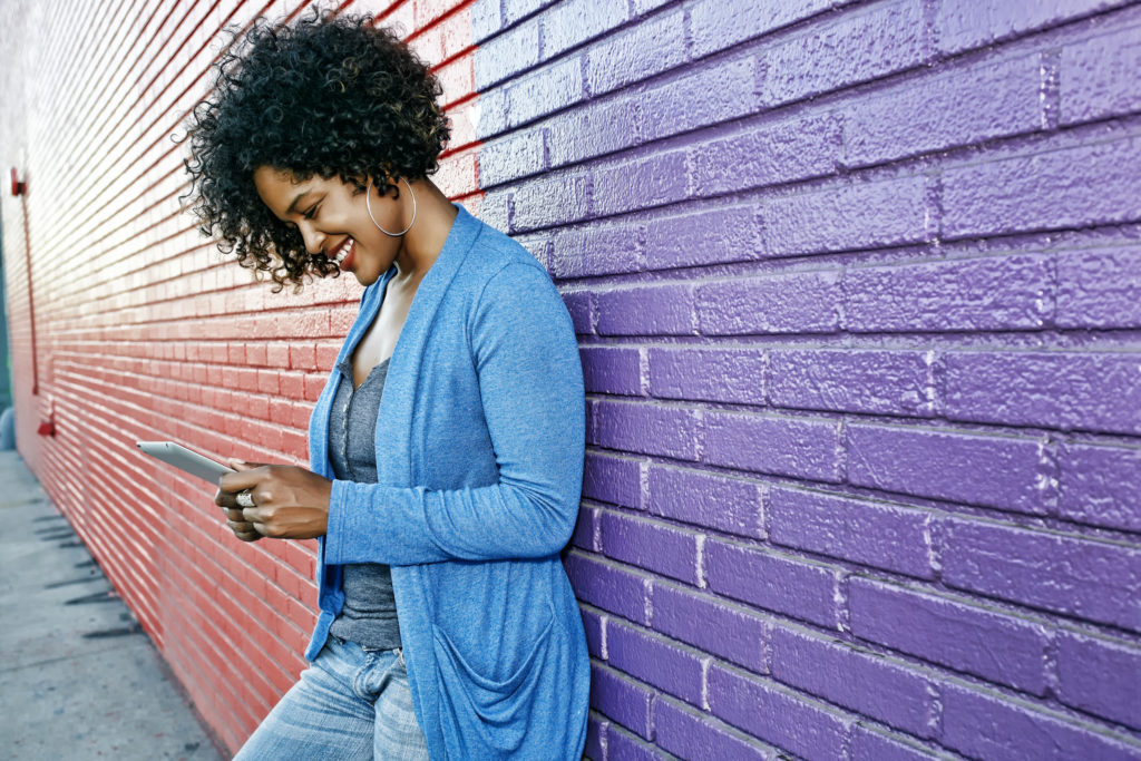 Happy smiling woman leaning against wall and using mobile phone while dating in Columbus, Ohio.