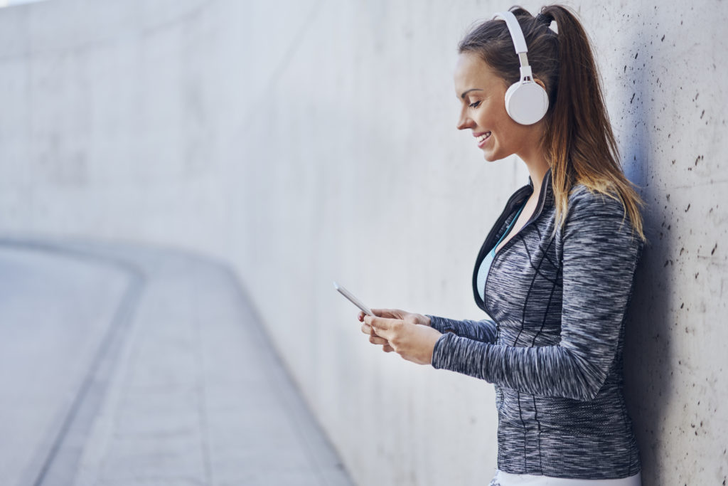 Happy woman wearing headphones and fitness clothes while using mobile to experience cop dating.