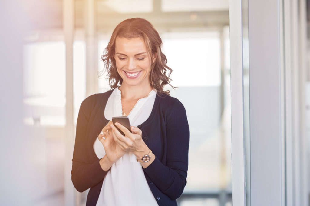 Smiling woman standing indoors while dating in Detroit and using mobile phone to connect with other Detroit singles.