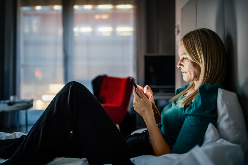 Woman relaxing on bed and using smartphone to connect with other singles while dating in Baltimore.
