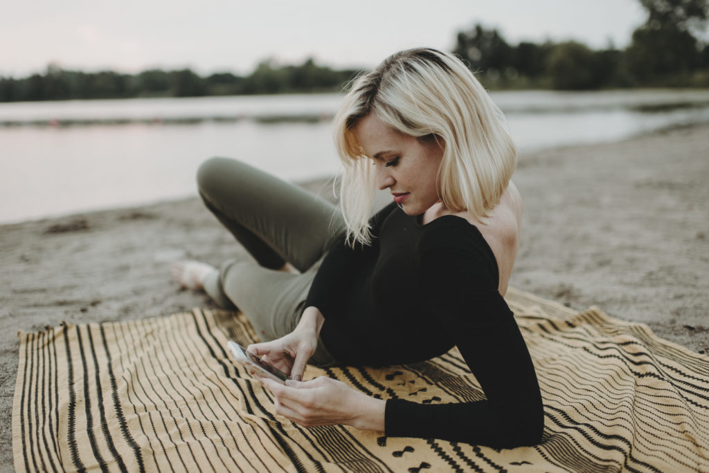 Young, smiling woman lying on the beach and using mobile phone for online dating in Minneapolis.