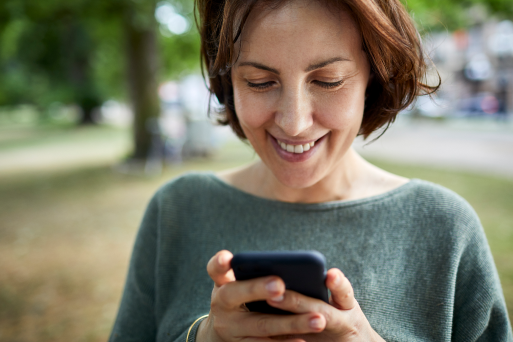 Happy, smiling woman walking down the street and using mobile phone for online dating in Rochester NY.