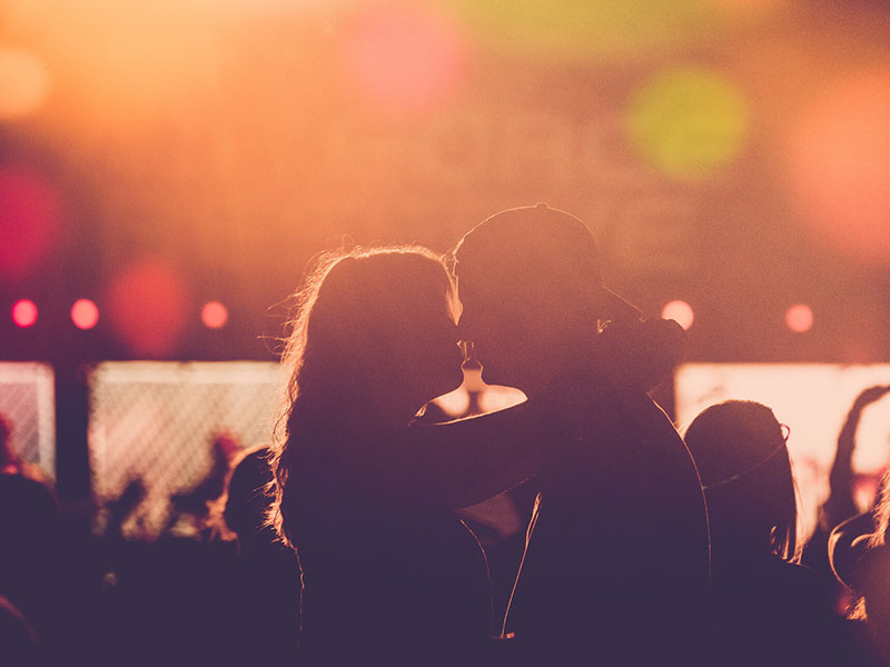 A couple in a healthy relationship kissing at a concert after going on a great date night.