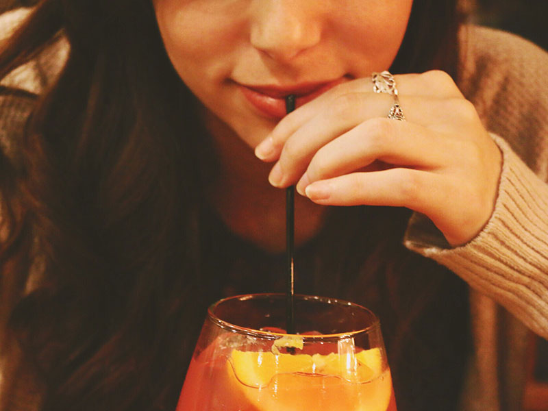 A woman sipping a drink at a bar to get a man to come to her.