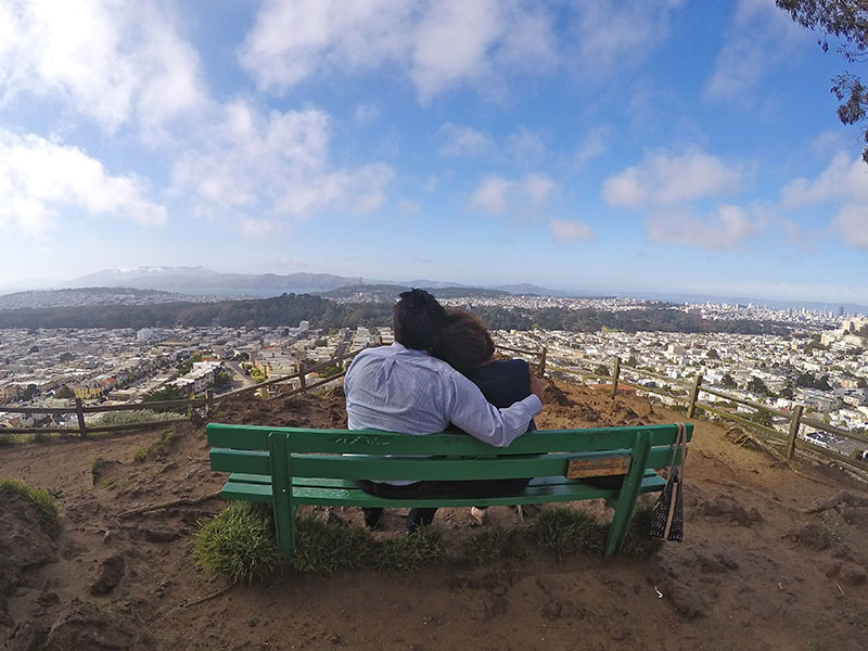 A couple dating after 50 sitting on a bench looking over a city.