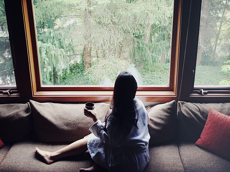 A woman who's getting over a divorce looking out her window drinking tea.