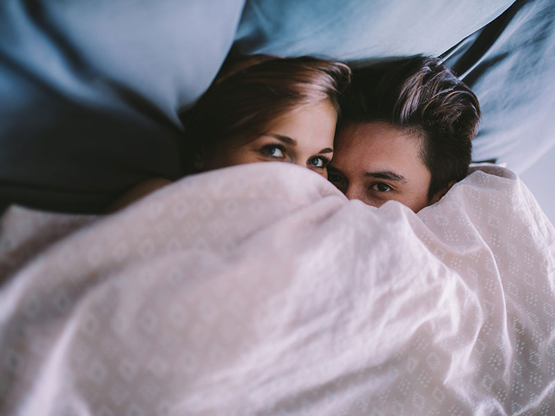 A couple hiding in bed who took these dating tips for people living at home into consideration.