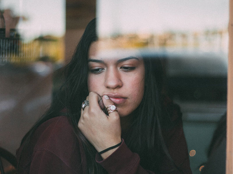 A girl looking sad out a window wondering to herself why can't I get over my ex.